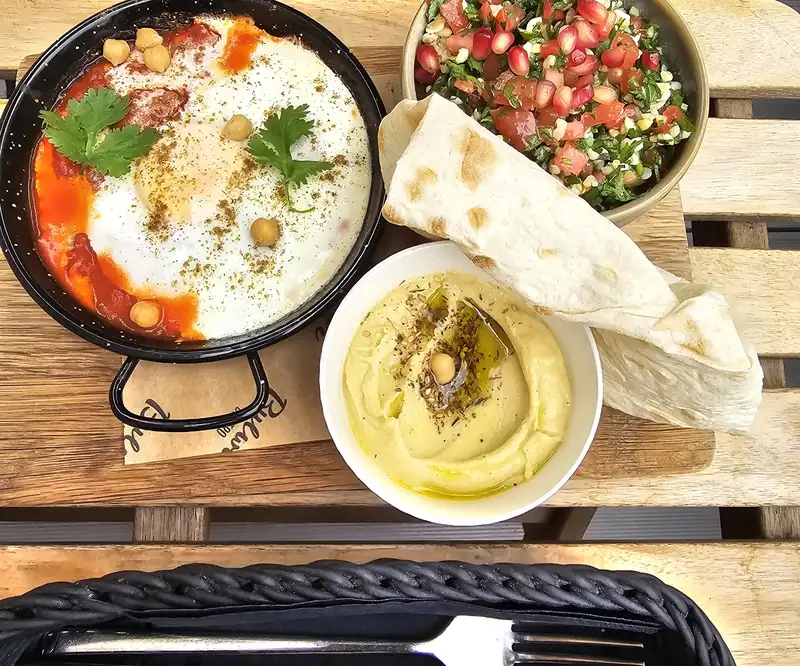 Szakszuka na patelni, hummus, tabbouleh i placki na drewnianej desce